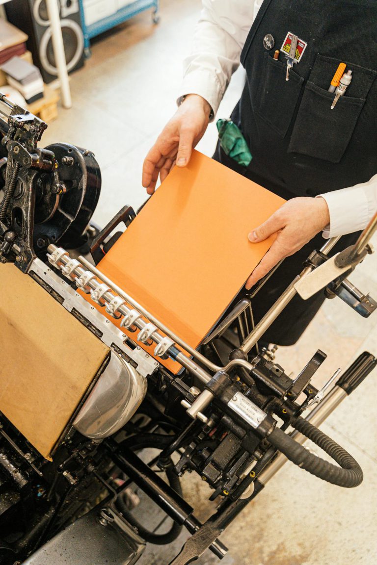 A person binding an orange book with craft equipment in a studio.